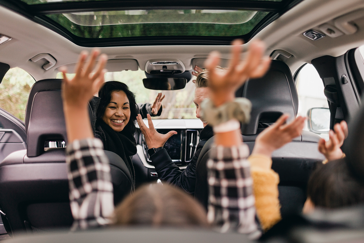 "cherrful family raising hands while enjoying road trip in car"