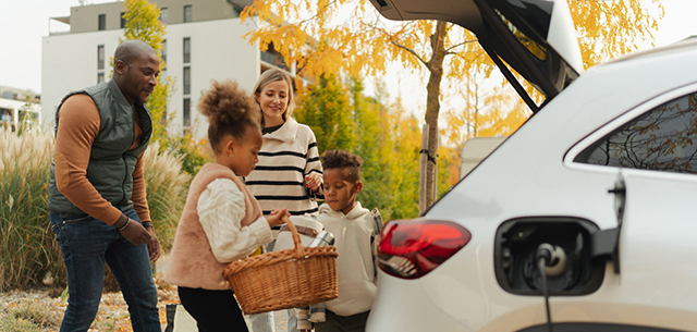 Cheerful multiracial family preparing for autumn picnic during their electric car charging.