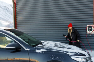 Woman with electric plug standing by car at vehicle charging station